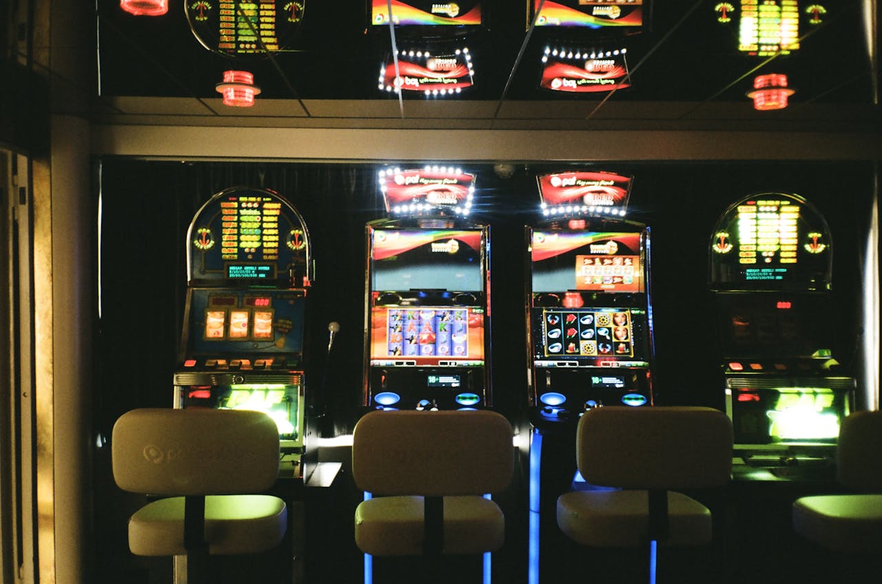 home-hero Slot machines in a dimly lit casino with reflective ceiling and empty chairs.
