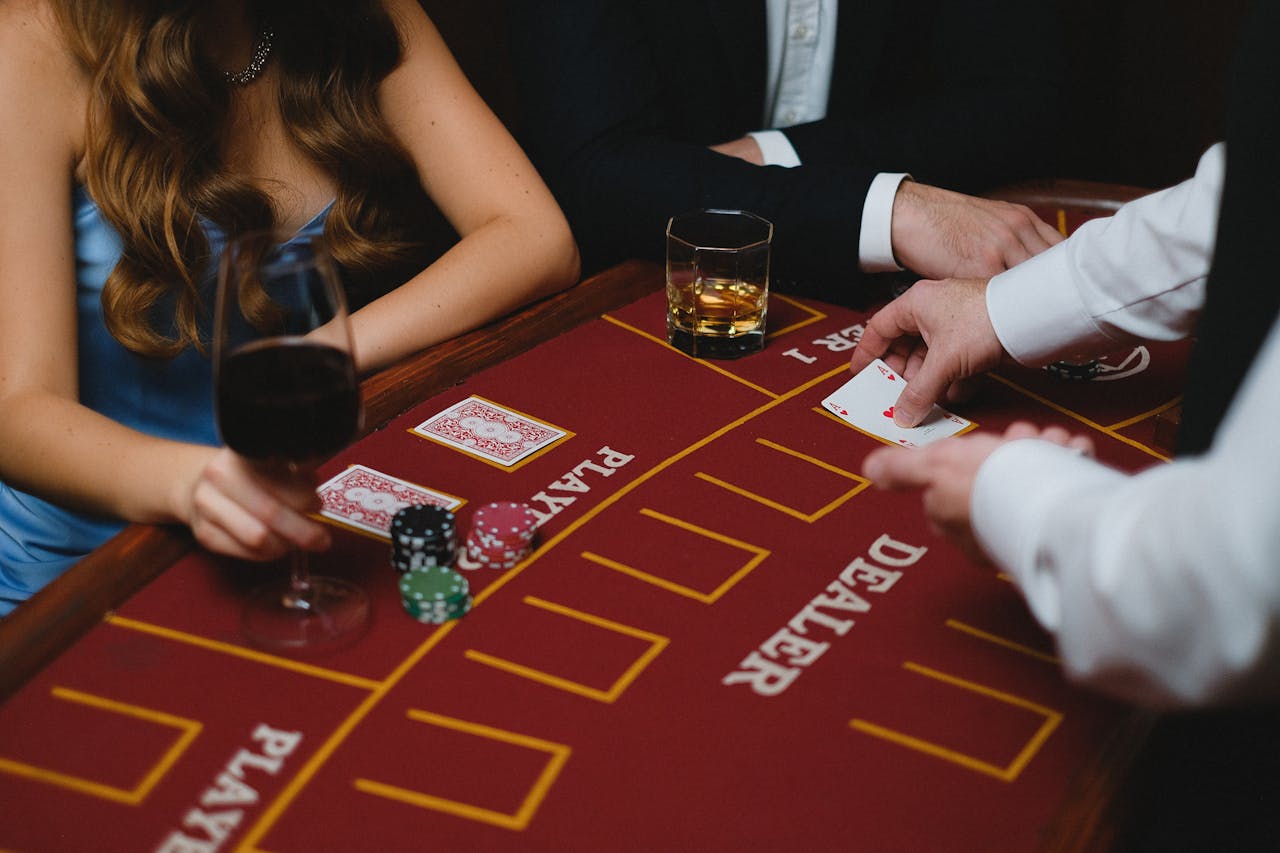 Close-up of a card game with players and chips at a casino table, featuring wine and whiskey glasses.