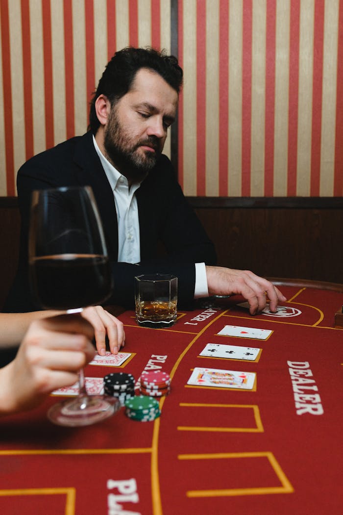 A man concentrating on a poker game at a casino table with cards, chips, and drinks.