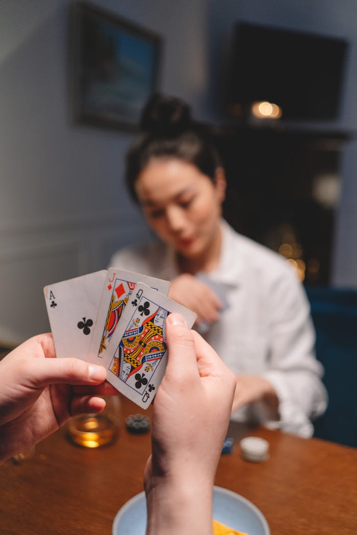 about-bg Focused close-up of a person holding cards during a poker game with a blurred background.