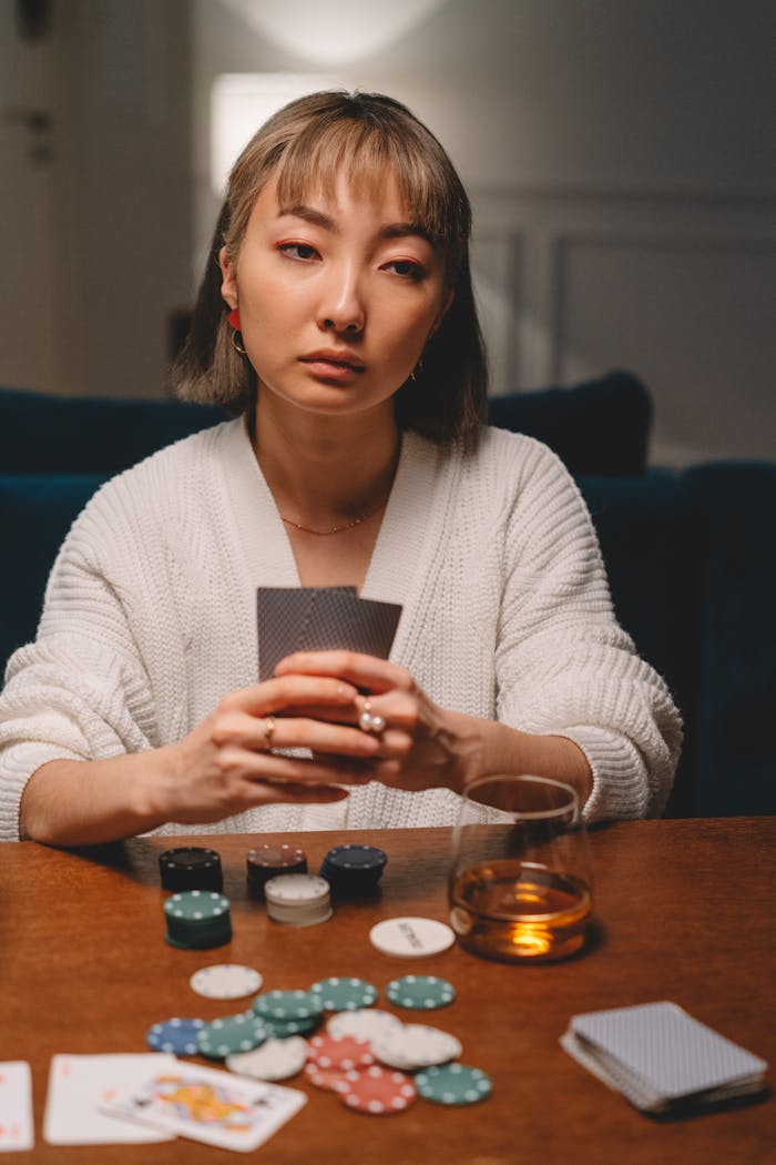 who-we-are An Asian woman playing poker at home, focused and serious, showcasing a strategic mindset.